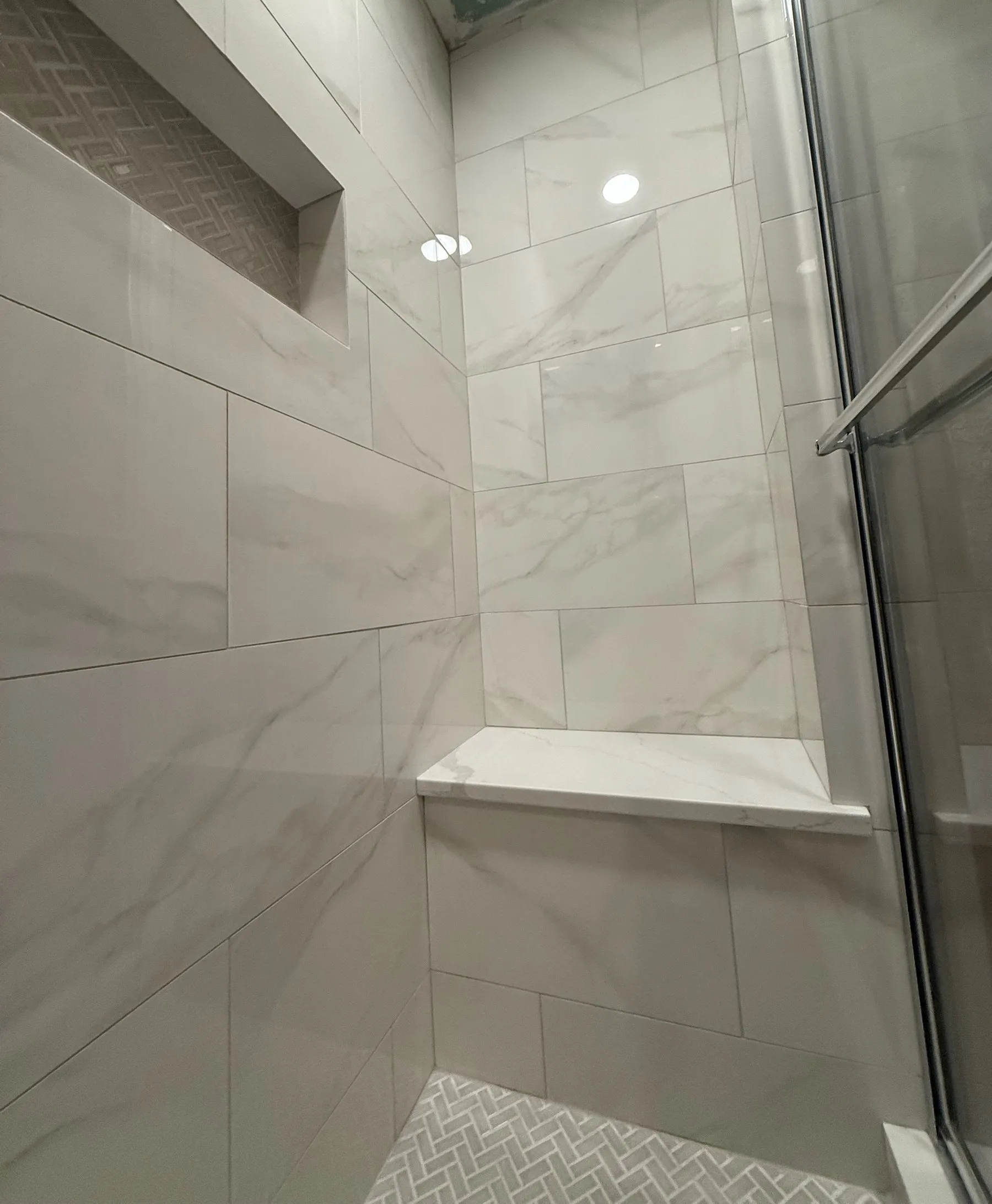 A marble-look shower with a built-in bench and a herringbone niche and floor