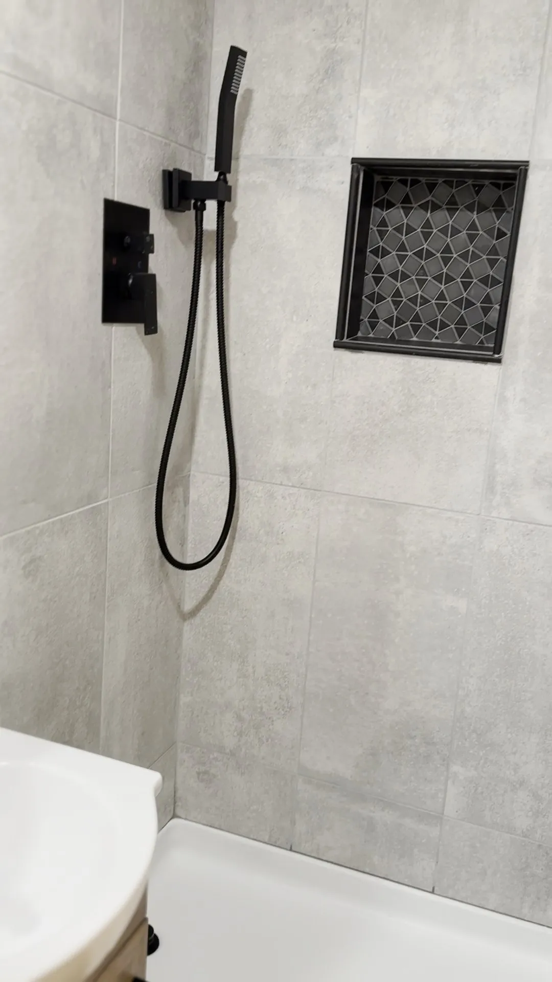 Gray tile, a matte black handheld shower and a patterned niche